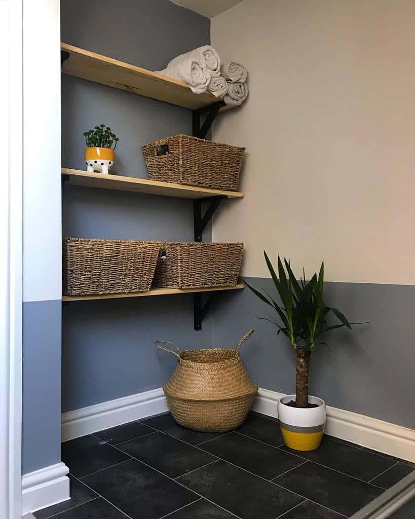 Corner storage with three wooden shelves holding woven baskets, a small plant, and rolled towels above a plant and a basket on a tiled floor