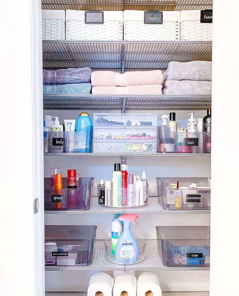 Organized linen closet with towels, woven baskets, and various toiletry items in labeled clear bins on metal shelves