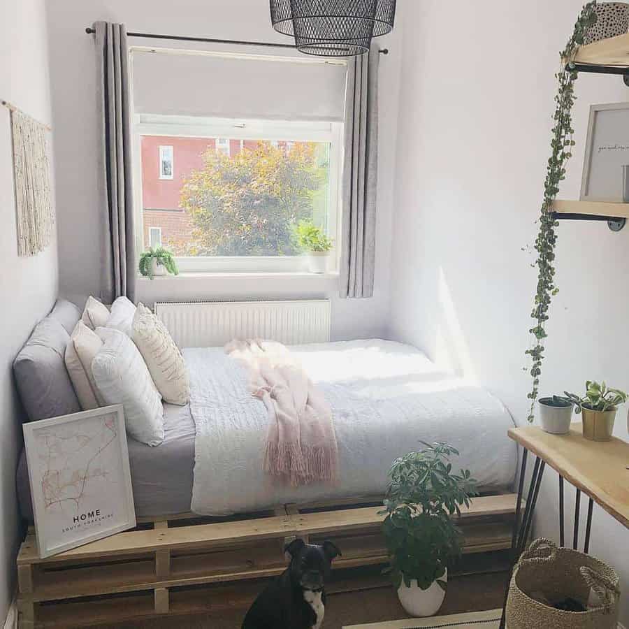 Minimalist bedroom with a cozy pallet bed frame, soft neutral bedding, natural light, indoor plants, and a small dog adding charm