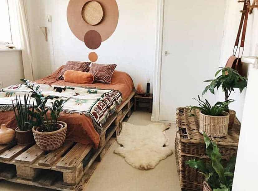 Boho-style bedroom with a rustic pallet bed frame, earthy-toned bedding, woven decor, indoor plants, and a cozy sheepskin rug