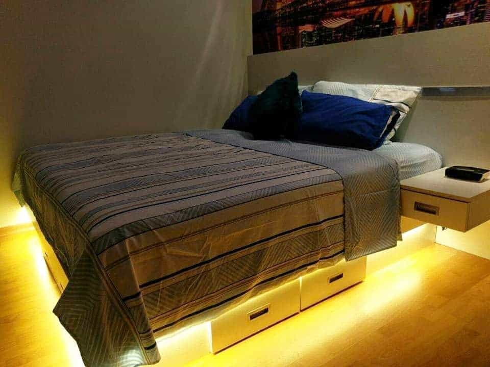 Modern bed with built-in storage drawers and warm LED lighting underneath, paired with floating nightstands for a sleek, space-saving design