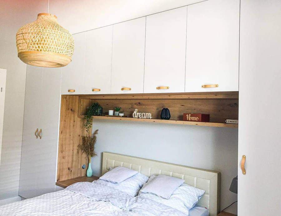 Cozy bedroom with a bed, overhead cabinets, wooden accents, decorative items, and a woven pendant light