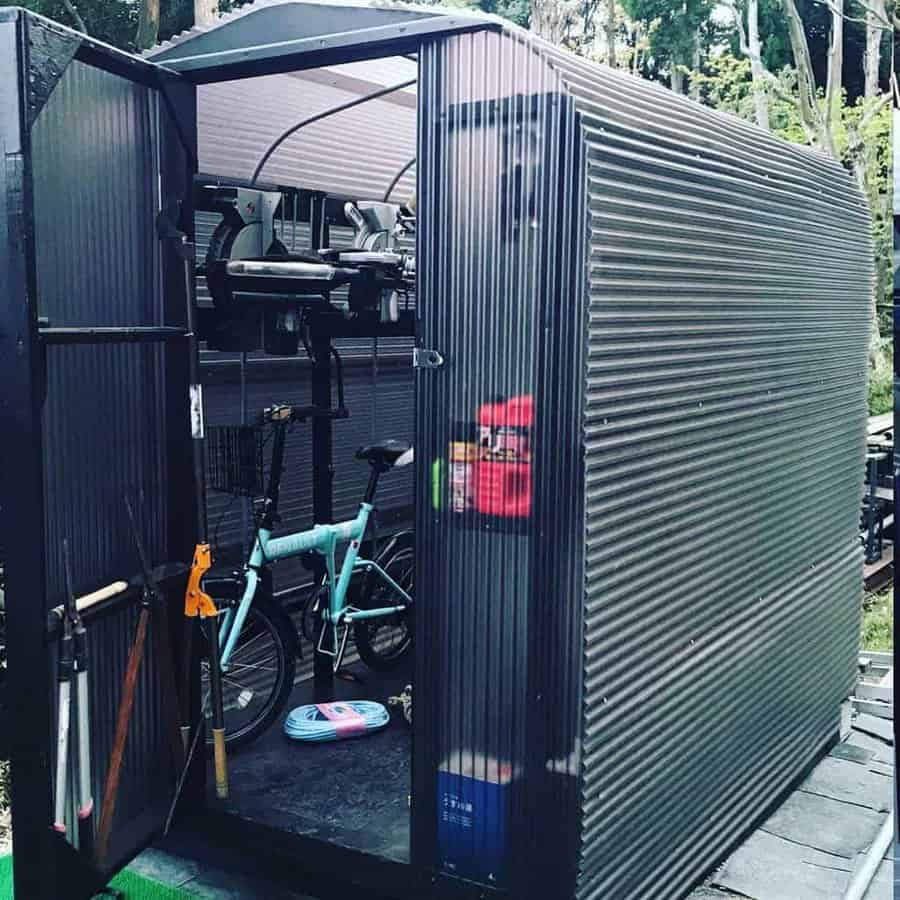 Small corrugated metal shed with an open door, showing a bicycle and shelves inside, tools and a fire extinguisher are visible