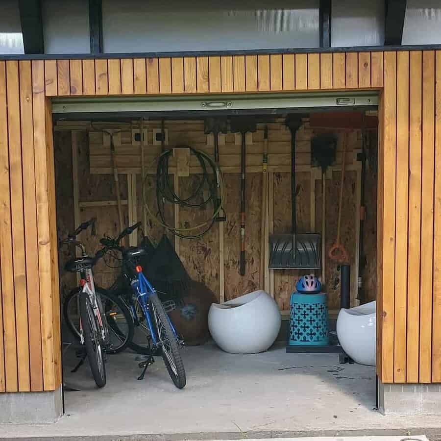 A wooden shed with bicycles, garden tools, a blue helmet, and large white planters inside