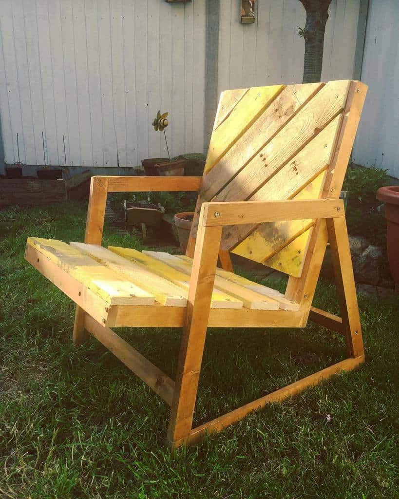 Handmade wooden pallet chair with a modern angled frame and diagonal slat backrest, placed on a grassy lawn in a cozy backyard