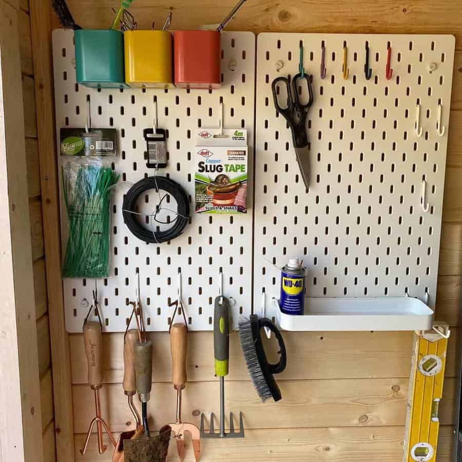 A pegboard holding various gardening tools, scissors, colorful containers, and a can of WD-40 with a small shelf holding more items