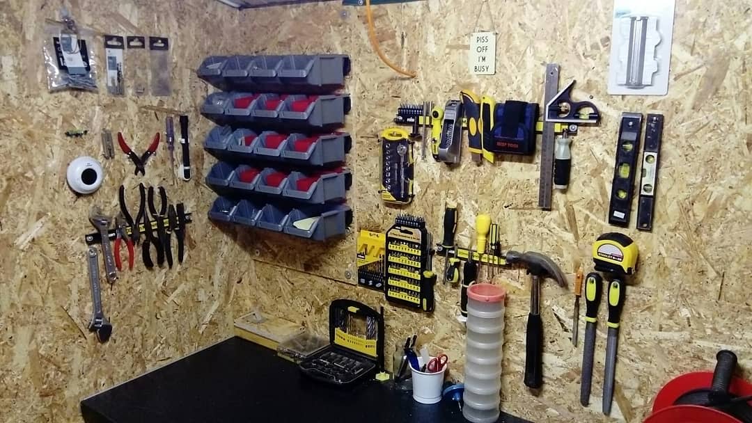 Wall-mounted tools and supplies organized neatly on a wooden board in a workshop, including pliers, screwdrivers, and a hammer