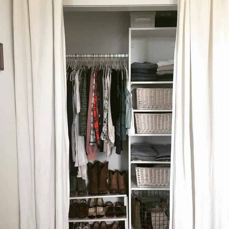 Open closet with hanging clothes, folded garments on shelves, shoes below, and baskets for storage; white curtains frame the space