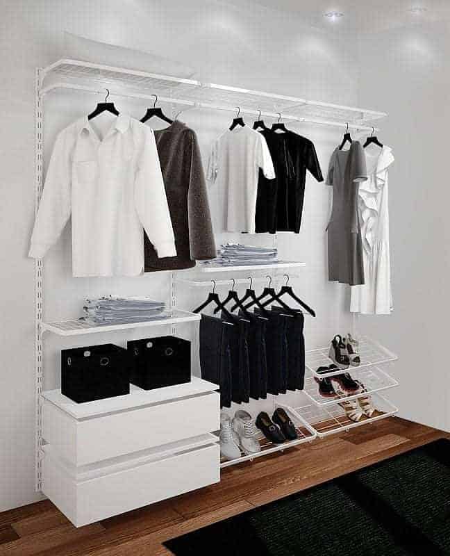 Minimalist wardrobe featuring hanging clothes, neatly folded jeans, and shoes on white shelves and drawers against a wooden floor with overhead lighting