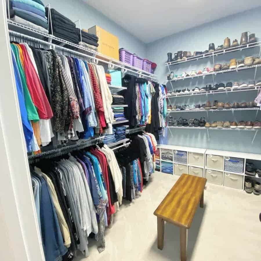 A neatly organized walk-in closet with clothes on hangers, folded garments, a variety of shoes on shelves, and a wooden bench in the center