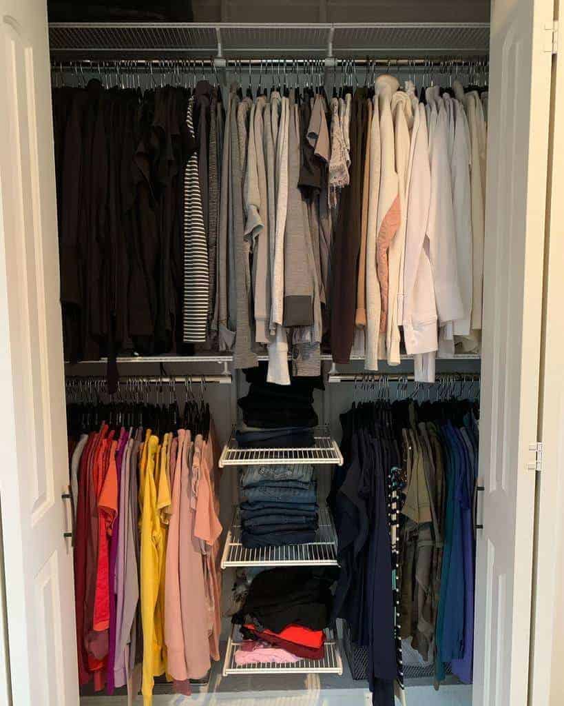 A neatly organized closet with clothes arranged by color, from dark to light. Shelves have folded jeans and other garments