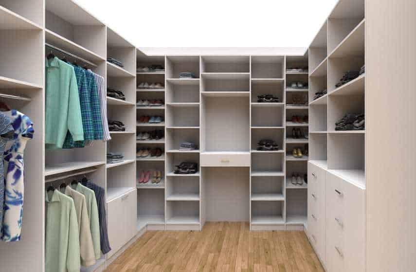 Walk-in closet with wooden flooring, featuring shelves filled with shoes, folded clothes, and hanging garments on both sides