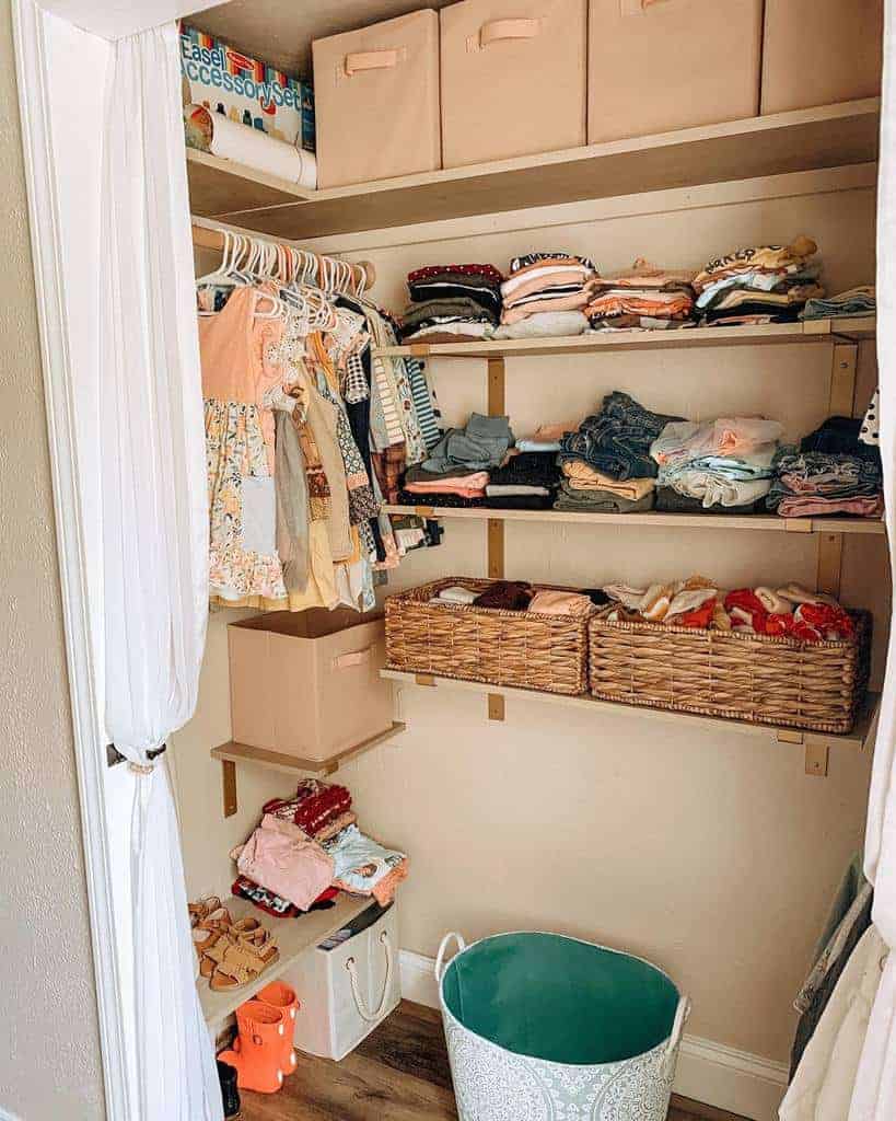 Organized closet with clothes hanging and folded on shelves, storage baskets, and a green laundry basket on the floor