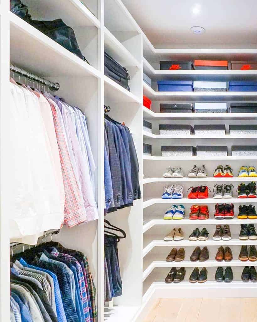 A neatly organized walk-in closet with shirts, jackets, and a variety of shoes arranged on white shelves