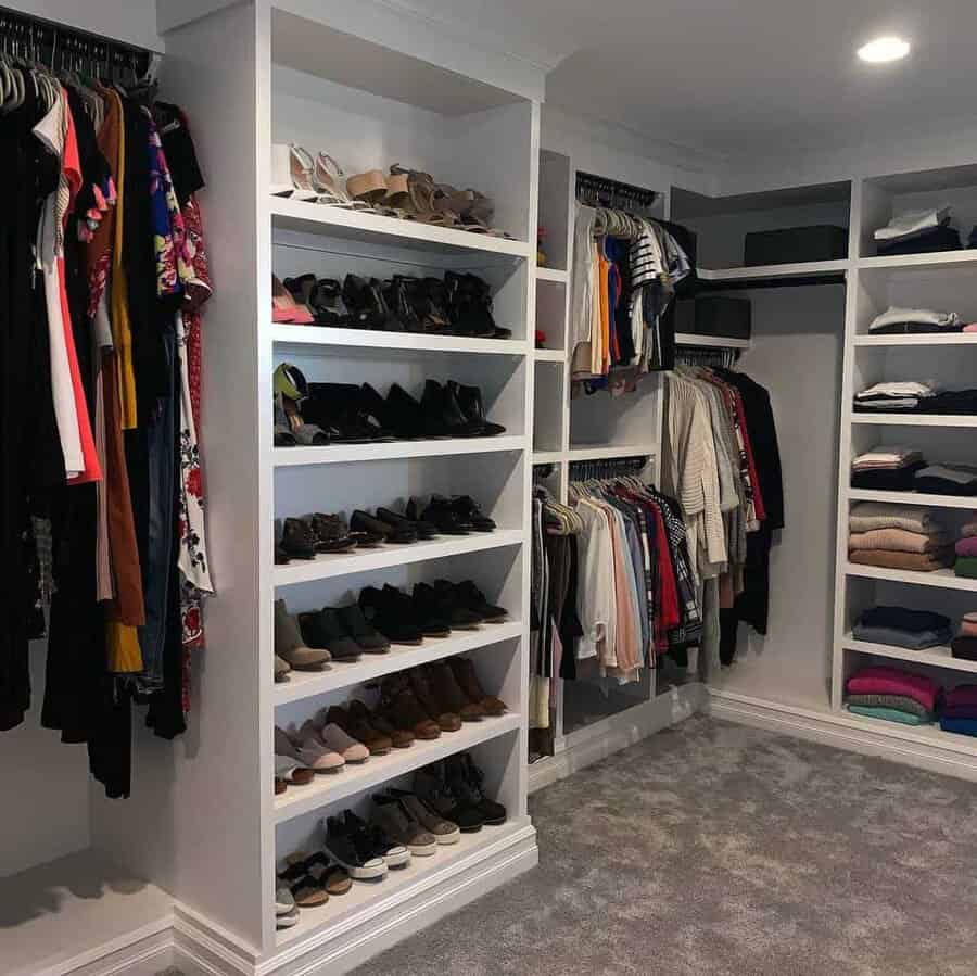 Walk-in closet with organized shelves of shoes, hanging clothes, and folded garments on racks against a carpeted floor