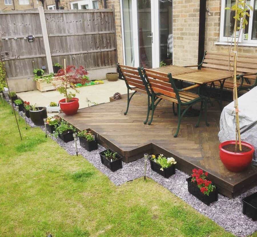 Modern backyard pallet deck with wooden benches, a dining table, potted plants, and a border of flower beds for a cozy outdoor setup