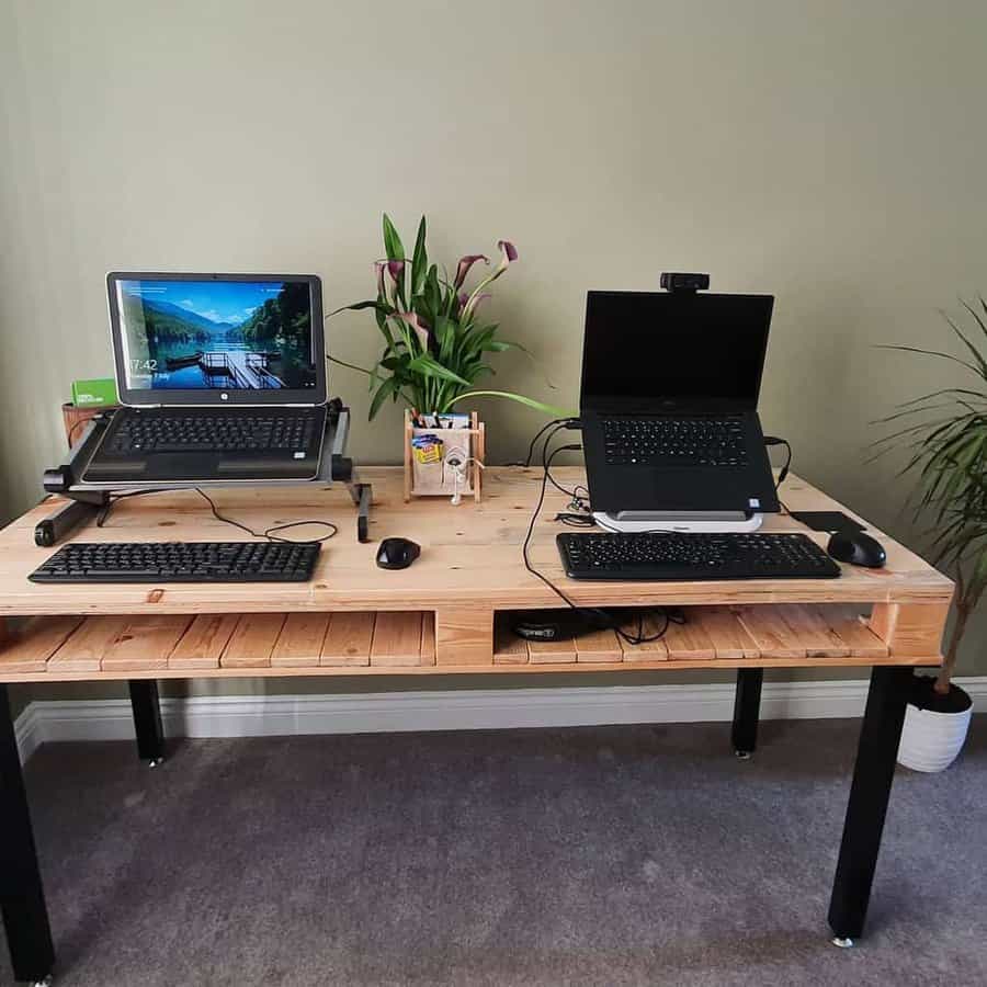 Spacious pallet desk with built-in storage, black metal legs, and a dual laptop setup, complemented by greenery in a modern home office