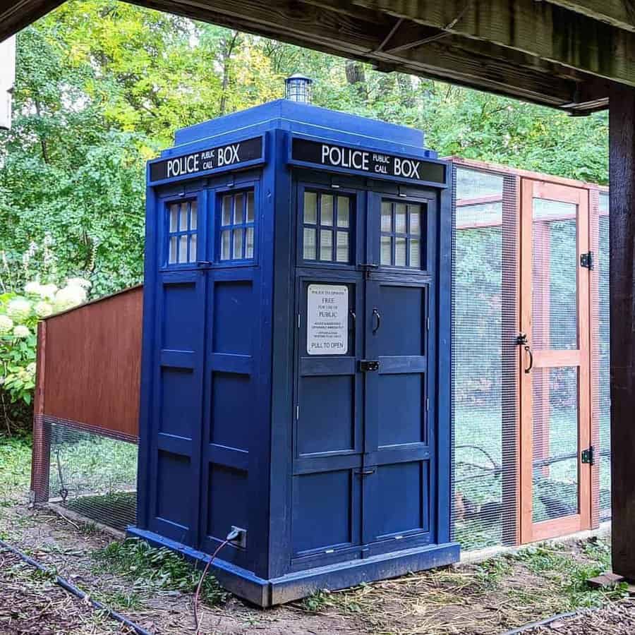 TARDIS-themed chicken coop painted deep blue, designed to resemble the iconic police box, with an attached mesh-enclosed run