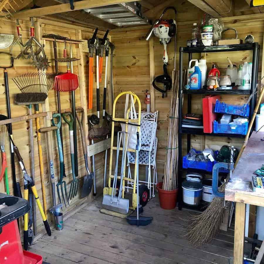 A tidy garden shed with various tools on walls and shelves, including rakes, shovels, and gardening supplies