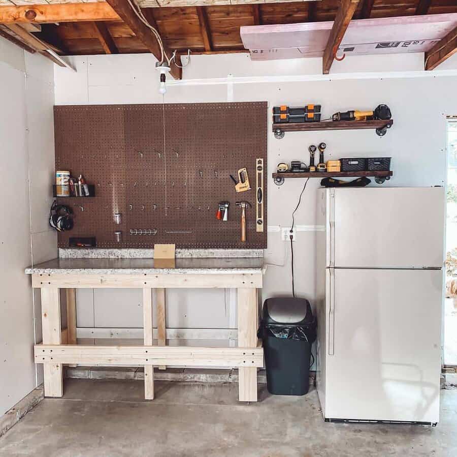 A tidy garage workspace with a wooden workbench, pegboard with tools, shelves with storage, and a white refrigerator