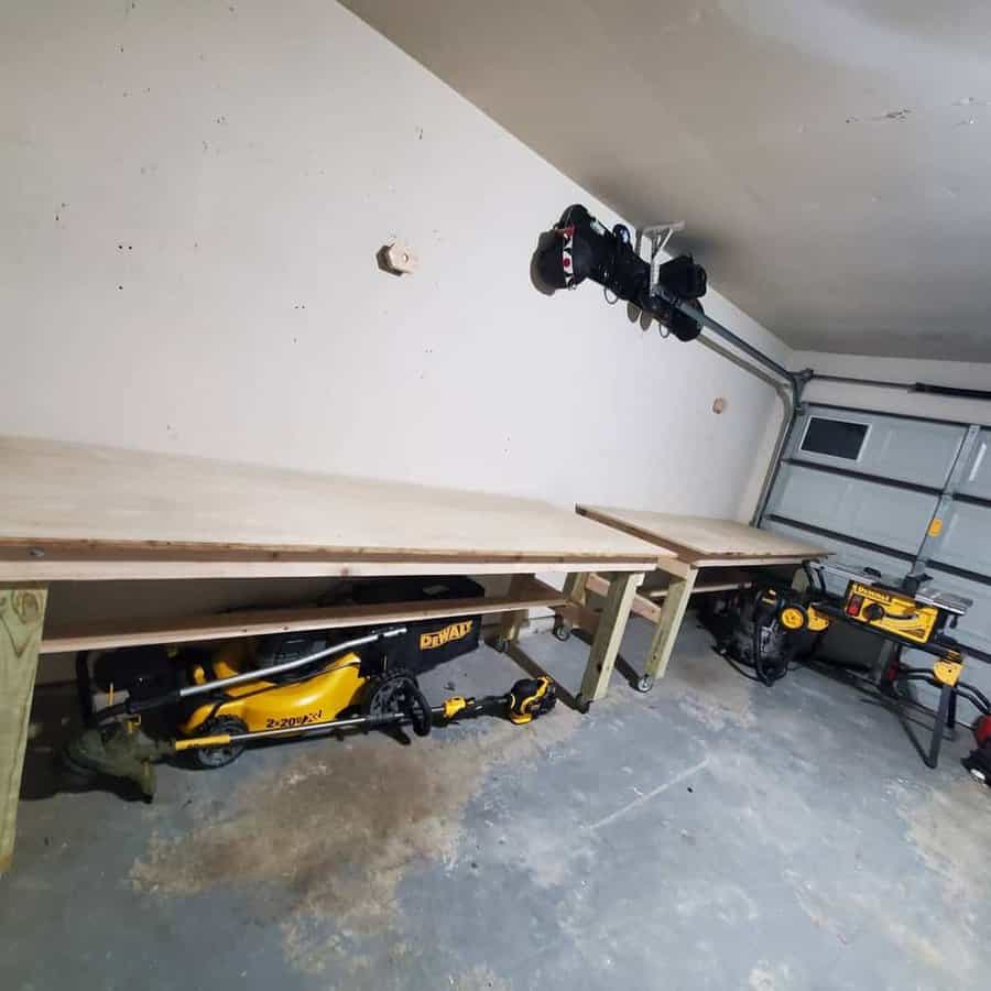 Two wooden workbenches in a garage with power tools underneath, and a garage door partially visible on the right