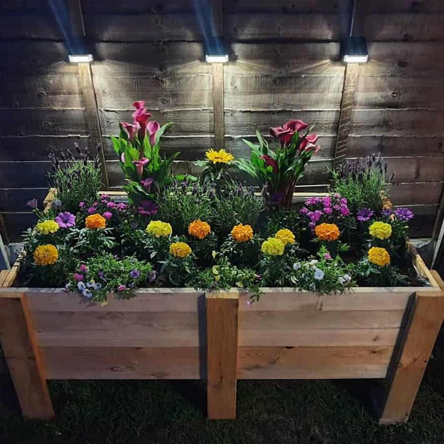 Beautiful DIY pallet planter box filled with vibrant flowers, illuminated by soft outdoor lights against a rustic wooden fence at night