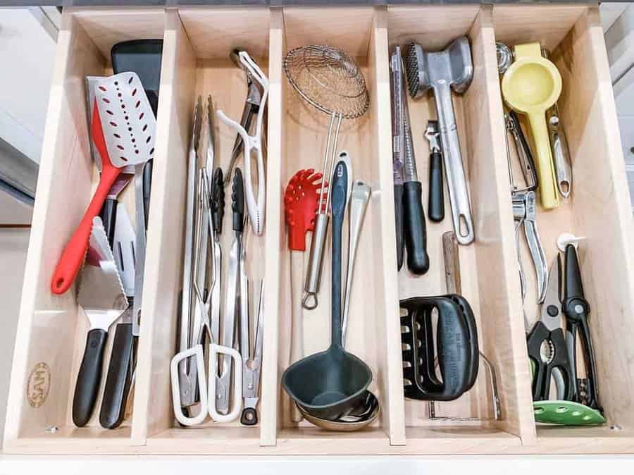 Kitchen drawer with neatly organized utensils, including spatulas, tongs, a whisk, soup ladle, lemon squeezer, and meat tenderizer