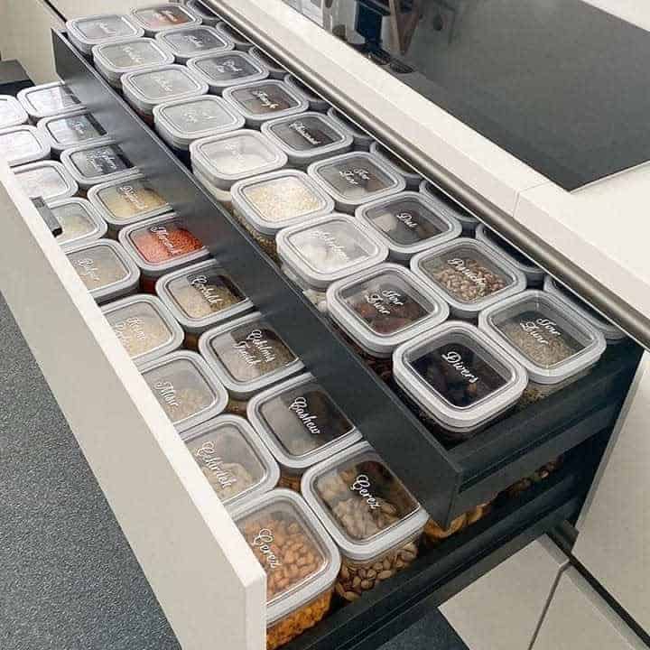 Neatly organized kitchen drawers with labeled containers filled with various dry ingredients and snacks