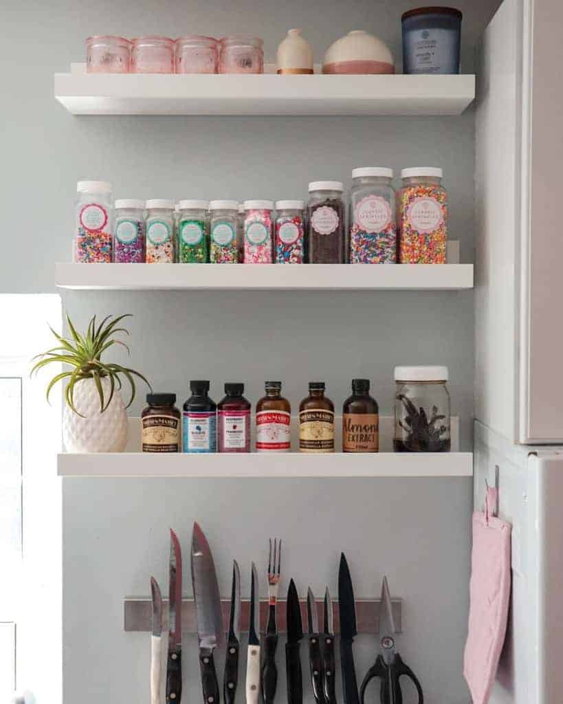 Kitchen shelves with jars of sprinkles, extracts, a plant, and hanging knives and scissors