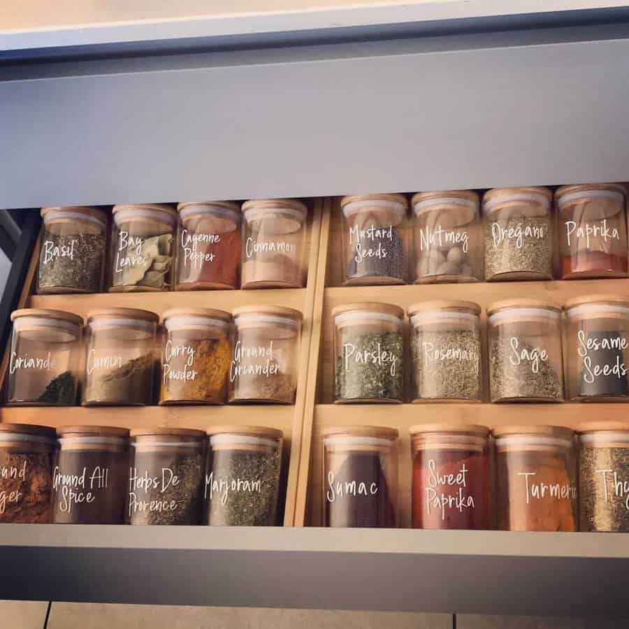 Open drawer with neatly arranged jars of spices and herbs, each labeled, including basil, cumin, coriander, and paprika