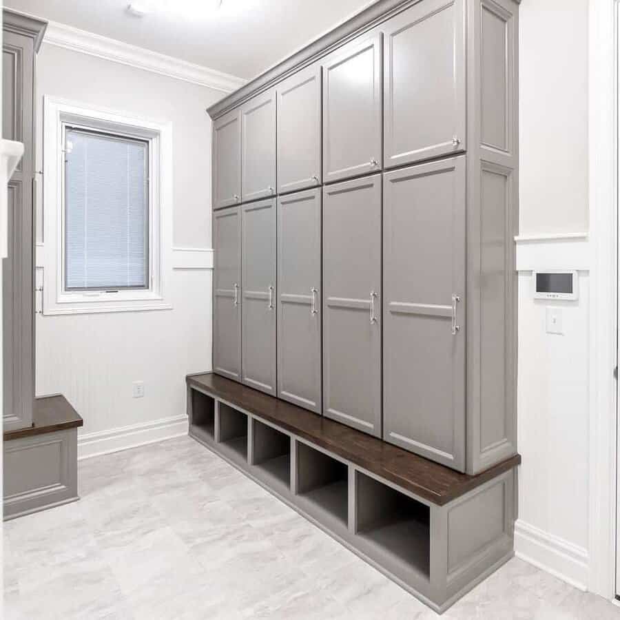 A room with tall gray cabinets, window, and a wooden bench with open storage cubes underneath