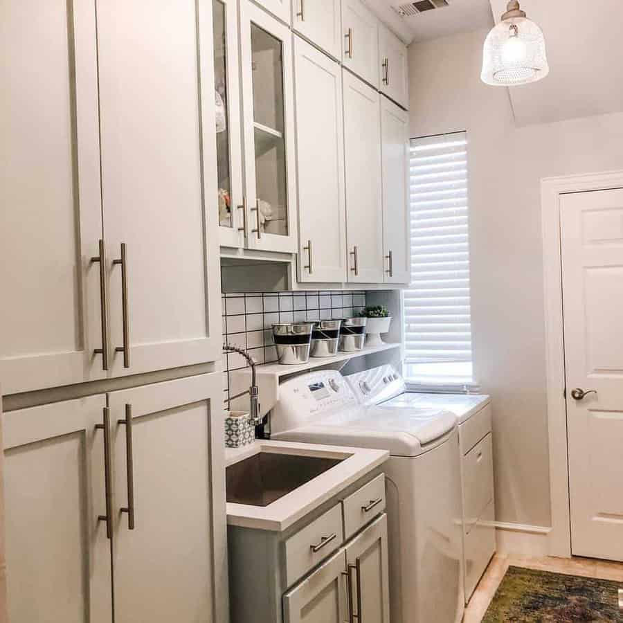 Modern laundry room with white cabinets, a washing machine, dryer, a small sink, and a vertical window with blinds