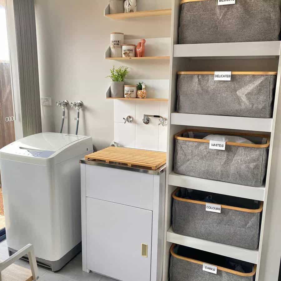 Modern laundry room with a washing machine, sink, shelves with jars, and labeled laundry baskets for sorting clothes