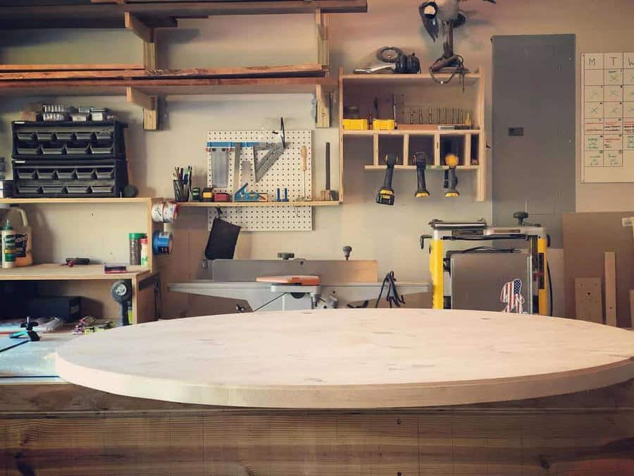 Woodworking shop with tools on shelves, a pegboard, a circular wooden table, and a wall calendar