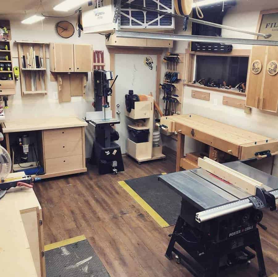 Woodworking shop with tools, workbenches, a table saw, and clamps on the wall, organized with wooden cabinets and shelves