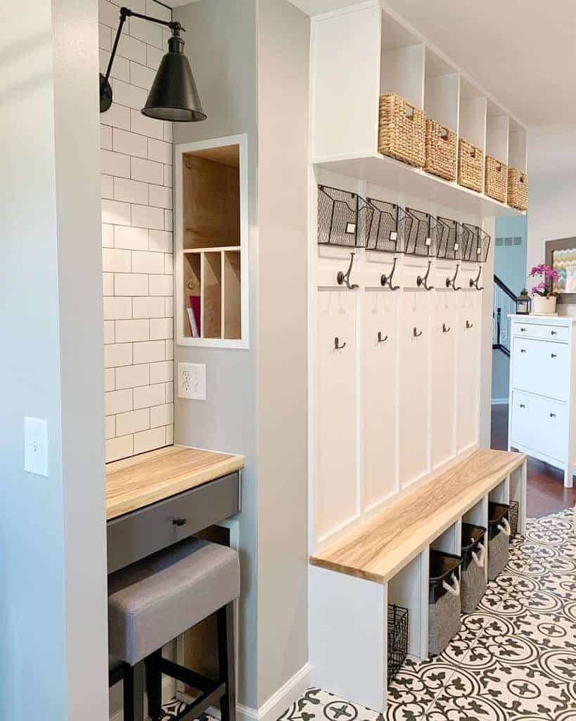 Bright mudroom with tiled floor, wooden bench, storage baskets, hooks on the wall, and a small desk with a stool in the corner