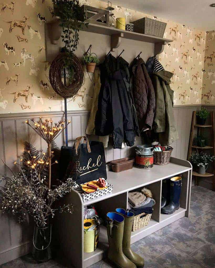 Cozy mudroom with coats hanging, boots on the floor, a shelf with baskets, and dog-themed wallpaper; string lights and plants decorate