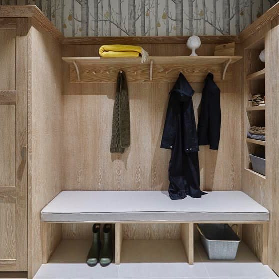 Mudroom with wooden shelves, bench, hooks with coats and a scarf, boots and basket below; folded yellow towel on top shelf