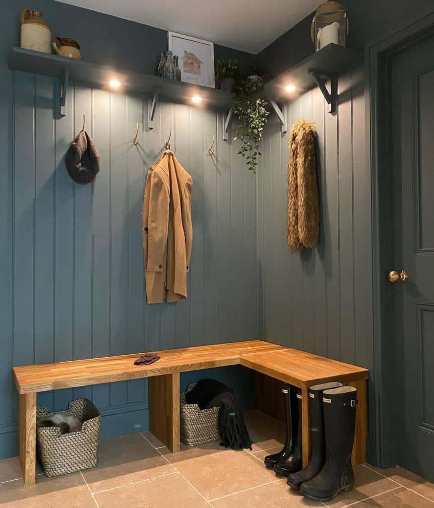 Mudroom with a wooden bench, coat hooks, dark walls, baskets underneath, boots, and a shelf with decor