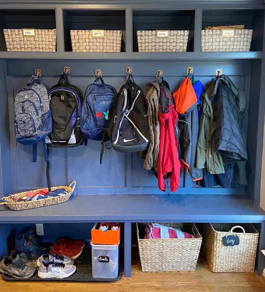 A blue mudroom with baskets on shelves, coats and backpacks hanging, and baskets of shoes on the floor