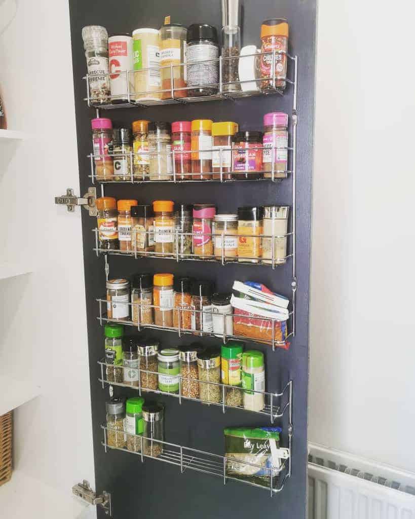 A pantry door with five shelves holding various spice jars and containers, organized and neatly arranged