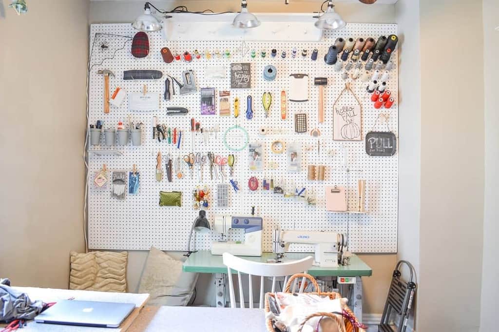 Craft room with a pegboard displaying various tools, threads, and supplies above a sewing machine and table with chairs