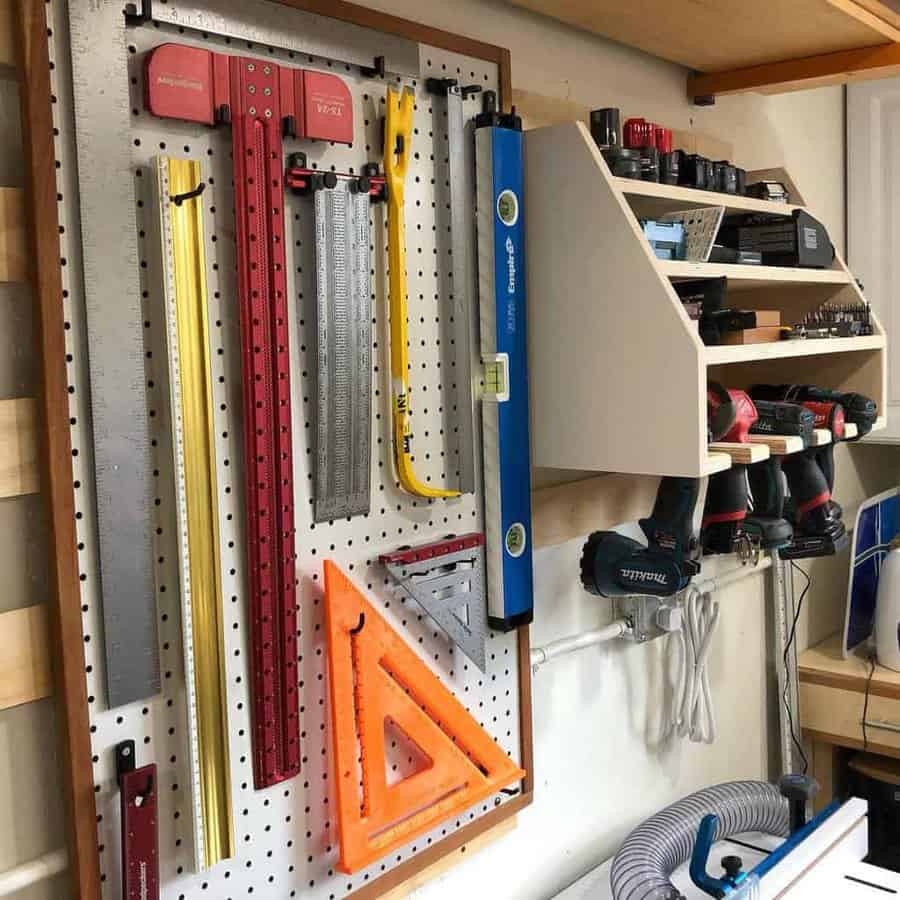 Workshop wall with a pegboard displaying various rulers and squares; shelves hold drills, batteries, and other tools and accessories