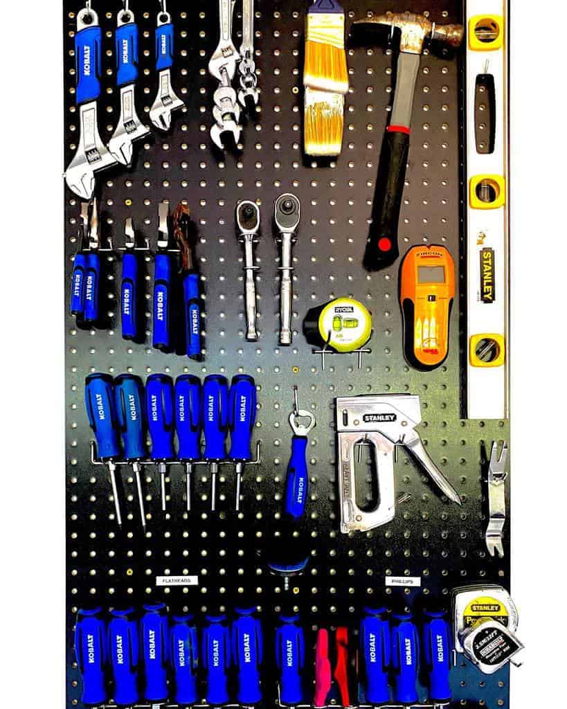 A pegboard with various hand tools, including screwdrivers, wrenches, a hammer, level, and tape measure, neatly organized