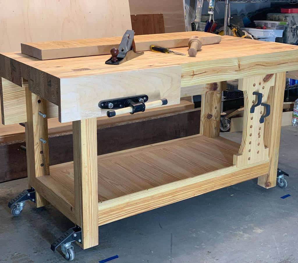 Wooden workbench on wheels with tools, including a hand plane and mallet, placed on top in a workshop setting