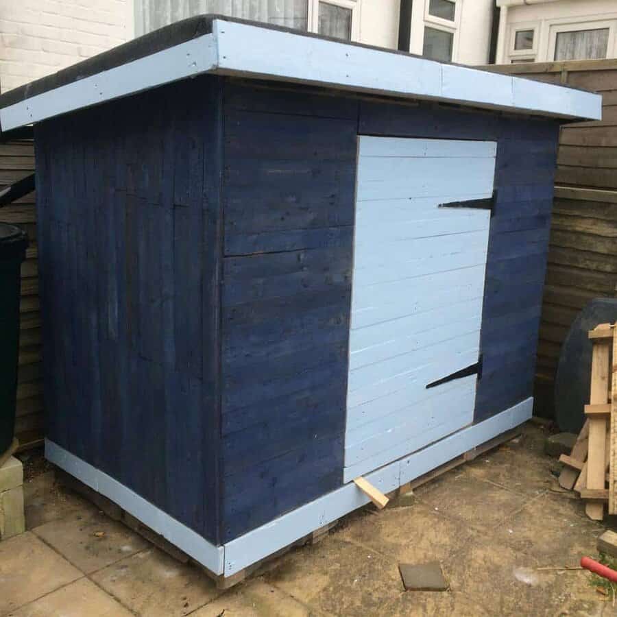 DIY pallet shed painted in dark and light blue, featuring a slanted roof and sturdy design on a paved surface