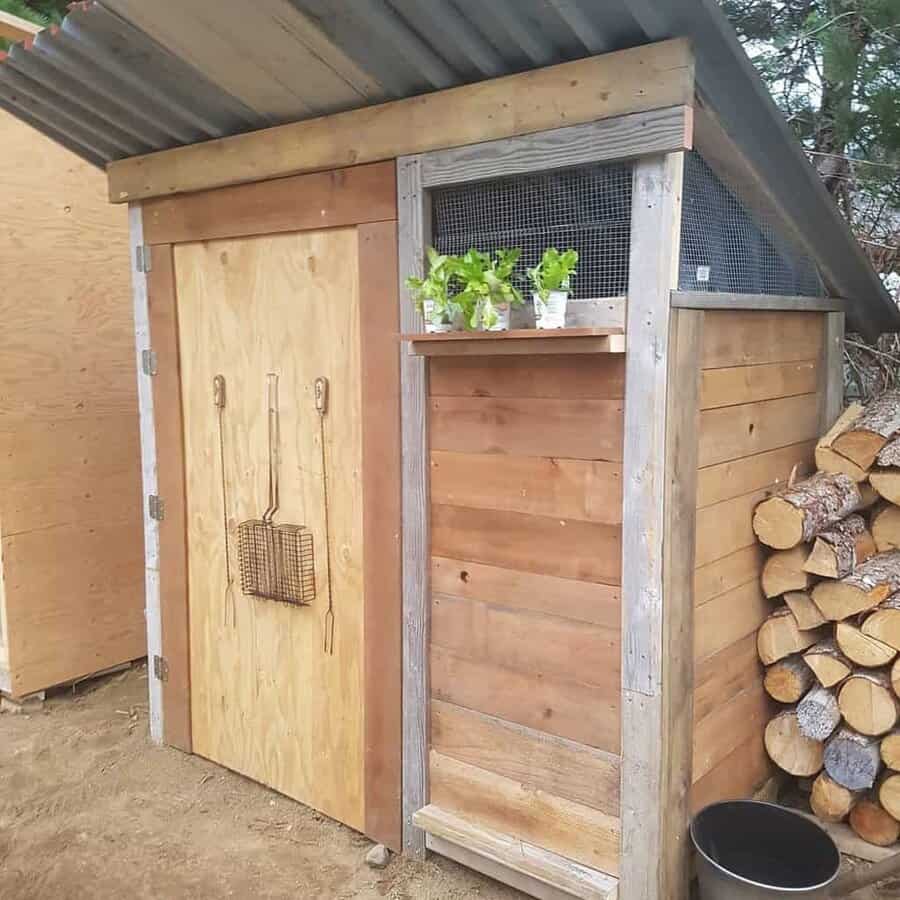 Rustic pallet shed with a slanted metal roof, wooden door, ventilation panel, and a side shelf for small plants