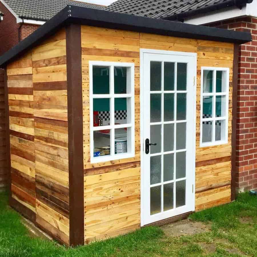 Stylish pallet shed with a modern touch, featuring a French door, two windows, and a mix of natural and stained wood panels