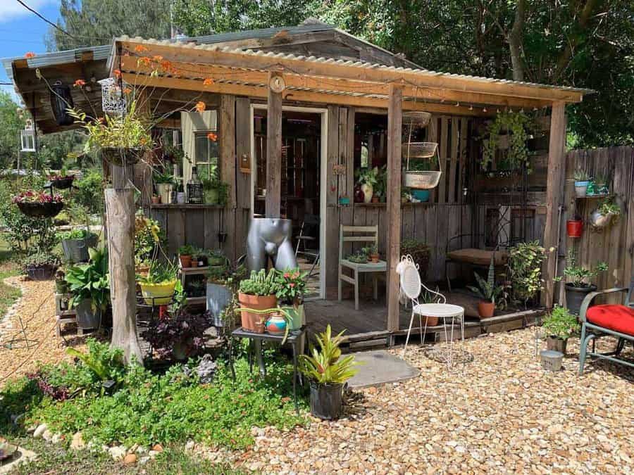 Rustic pallet shed with an open-air porch, lush greenery, and eclectic decor—perfect for a cozy backyard retreat or garden workspace