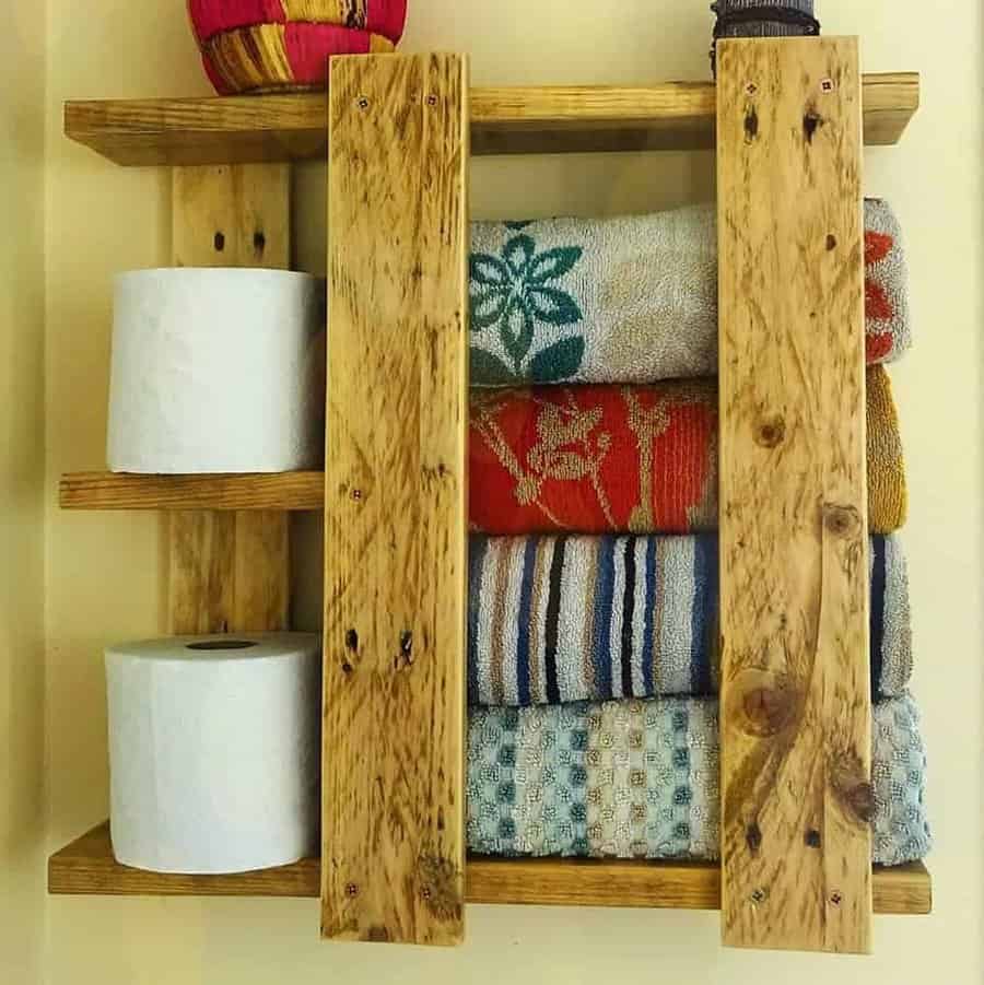 Rustic pallet wood shelf repurposed for bathroom storage, holding neatly folded towels and toilet paper rolls for a cozy, organized look